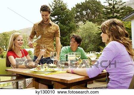 2 young smiling couples sitting at garden table, man pouring wine View Large Photo Image Stock Image - 2 young smiling couples sitting at garden table, man pouring wine. Fotosearch