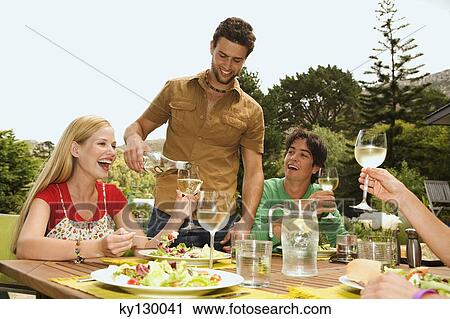 2 young smiling couples sitting at garden table, man pouring wine View Large Photo Image Stock Image - 2 young smiling couples sitting at garden table, man pouring wine. Fotosearch