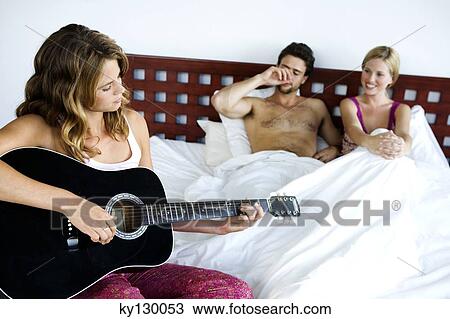 Young couple in bed listening to woman playing guitar View Large Photo Image Stock Image - Young couple in bed listening to woman playing guitar. Fotosearch