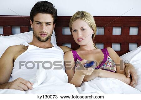 Stock Image - Young couple in bed, watching TV. Fotosearch