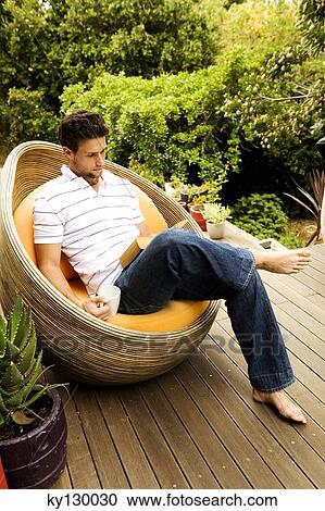Young man sitting in armchair reading a book, outdoors View Large Photo Image Stock Image - Young man sitting in armchair reading a book, outdoors. Fotosearch