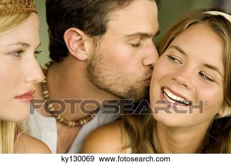 Young woman looking at man kissing smiling woman View Large Photo Image Stock Photo - Young woman looking at man kissing smiling woman. Fotosearch