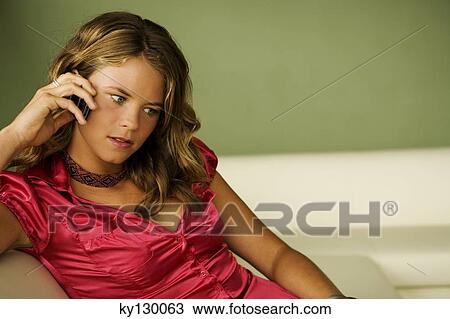 Young woman sitting on a sofa, using mobile phone View Large Photo Image Stock Image - Young woman sitting on a sofa, using mobile phone. Fotosearch