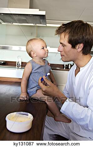 Father and son in kitchen, man feeding his baby, indoors View Large Photo Image Stock Photo - Father and son in kitchen, man feeding his baby, indoors. Fotosearch