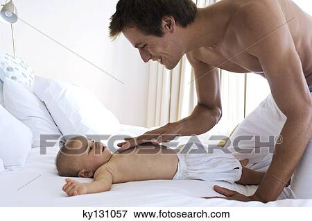 Father caressing chest's baby, lying on a bed, indoors View Large Photo Image Stock Photo - Father caressing chest's baby, lying on a bed, indoors. Fotosearch