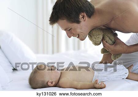Father looking at his baby, lying in bed, indoors View Large Photo Image Stock Photograph - Father looking at his baby, lying in bed, indoors. Fotosearch