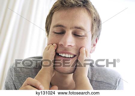 Father playing with his baby, feet on his cheeks, indoors View Large Photo Image Picture - Father playing with his baby, feet on his cheeks, indoors. Fotosearch