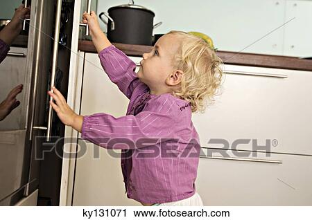 Stock Image - Littel girl opening fridge, indoors. Fotosearch