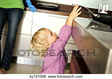Stock Photo - Little girl in kitchen trying to catch a frying pan on stove, indoors. Fotosearch