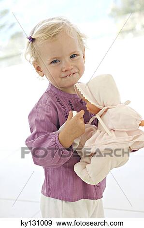 Stock Photo - Little girl looking at the camera, holding her doll, indoors. Fotosearch