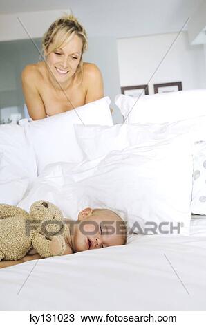 Stock Image - Mother smiling looking at her baby asleep, indoors. Fotosearch