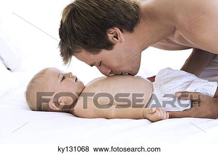 Portrait of a father kissing his baby's chest, lying on bed, indoors View Large Photo Image Stock Photo - Portrait of a father kissing his baby's chest, lying on bed, indoors. Fotosearch