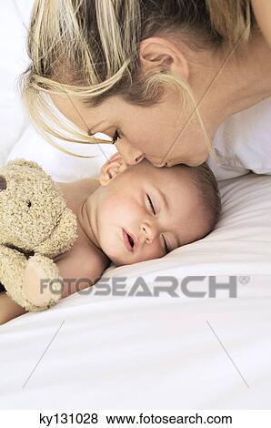 Stock Photo - Portrait of mother kissing her baby sleeping, indoors. Fotosearch
