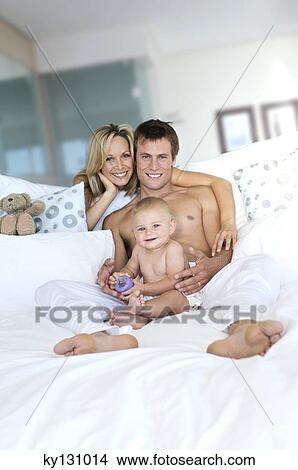 Young couple and baby in living room, looking at the camera, indoors View Large Photo Image Picture - Young couple and baby in living room, looking at the camera, indoors. Fotosearch