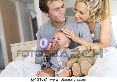 Young couple and baby in living room, father feeding his son, indoors View Large Photo Image Stock Image - Young couple and baby in living room, father feeding his son, indoors. Fotosearch