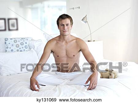 Young man sitting cross-legged on a bed, indoors View Large Photo Image Stock Photo - Young man sitting cross-legged on a bed, indoors. Fotosearch