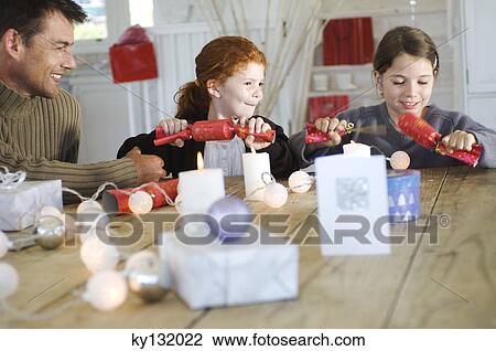 Christmas day, father and two daughters exchanging presents, sitting around table, indoors View Large Photo Image Stock Image - Christmas day, father and two daughters exchanging presents, sitting around table, indoors. Fotosearch