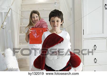Christmas day, little boy holding a cuddly toy (Santa Claus), looking at the camera, sister with present in background, indoors View Large Photo Image Stock Photo - Christmas day, little boy holding a cuddly toy (Santa Claus), looking at the camera, sister with present in background, indoors. Fotosearch