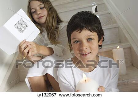 Christmas day, portrait of a little boy holding a candle, girl in background reading a card, indoors View Large Photo Image Stock Photo - Christmas day, portrait of a little boy holding a candle, girl in background reading a card, indoors. Fotosearch