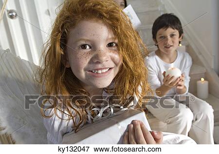 Christmas day, portrait of a little girl holding a present, little boy in background, indoors View Large Photo Image Stock Photo - Christmas day, portrait of a little girl holding a present, little boy in background, indoors. Fotosearch