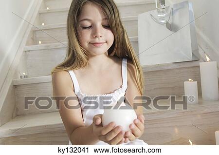 Stock Image - Christmas, little girl sitting indoors, holding a candle, indoors. Fotosearch