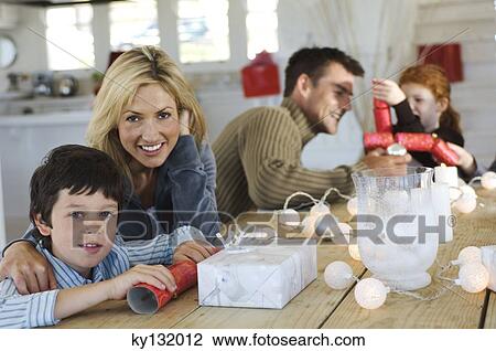 Couple ad three children sitting around table, exchanging Christmas presents, indoors View Large Photo Image Stock Image - Couple ad three children sitting around table, exchanging Christmas presents, indoors. Fotosearch