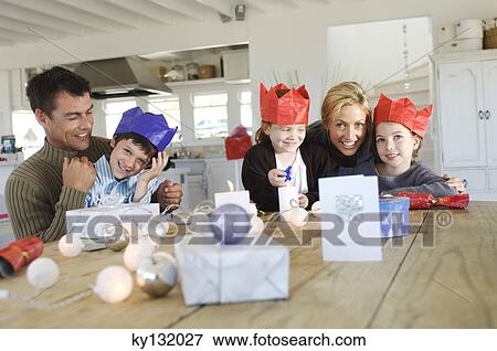 Couple ad three children sitting around table, exchanging Christmas presents, indoors View Large Photo Image Stock Photo - Couple ad three children sitting around table, exchanging Christmas presents, indoors. Fotosearch