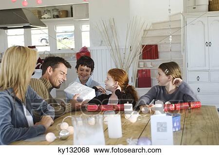 Couple ad three children sitting around table, exchanging Christmas presents, indoors View Large Photo Image Stock Photo - Couple ad three children sitting around table, exchanging Christmas presents, indoors. Fotosearch