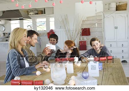 Couple ad three children sitting around table, exchanging Christmas presents, indoors View Large Photo Image Stock Photograph - Couple ad three children sitting around table, exchanging Christmas presents, indoors. Fotosearch