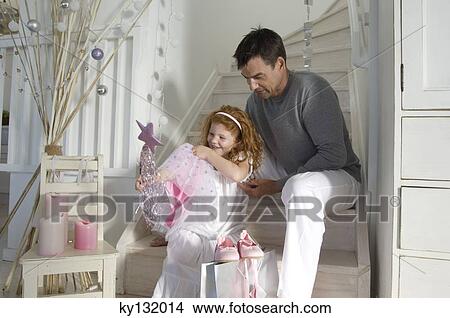 Father and daughter opening Christmas presents, girl holding a princess costume, indoors View Large Photo Image Picture - Father and daughter opening Christmas presents, girl holding a princess costume, indoors. Fotosearch