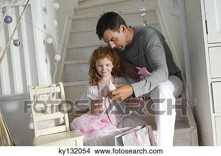 Father and ldaughter opening Christmas presents, girl holding a princess costume, indoors View Large Photo Image Picture - Father and ldaughter opening Christmas presents, girl holding a princess costume, indoors. Fotosearch