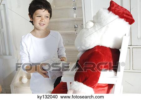 Little boy holding a present, looking at a cuddly toy (Santa Claus), indoors View Large Photo Image Stock Image - Little boy holding a present, looking at a cuddly toy (Santa Claus), indoors. Fotosearch