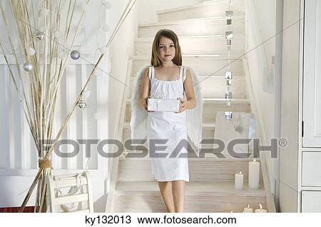 Stock Image - Little girl holding a Christmas present, indoors. Fotosearch