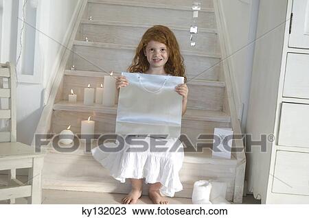 Stock Image - Little girl holding a Christmas present, indoors. Fotosearch