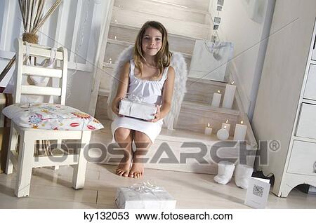 Stock Image - Little girl holding a Christmas present, indoors. Fotosearch
