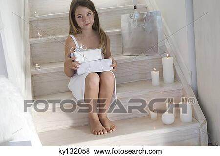 Stock Photo - Little girl holding a Christmas present, indoors. Fotosearch