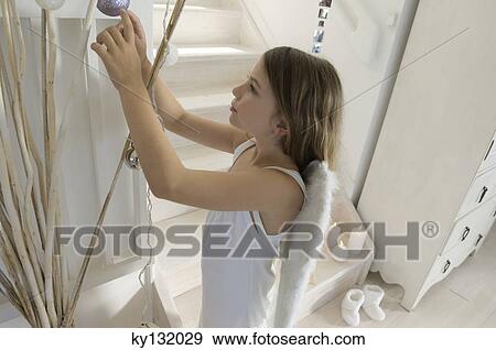 Little girl in a angel costume decorating branches with Christmas balls, indoors View Large Photo Image Stock Photo - Little girl in a angel costume decorating branches with Christmas balls, indoors. Fotosearch