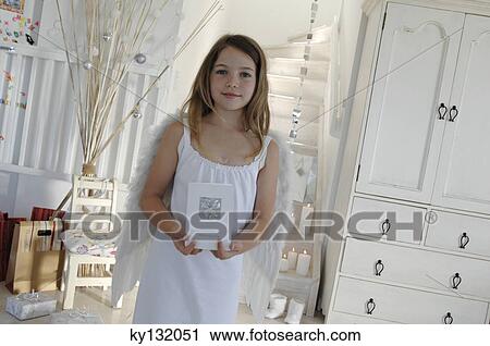 Stock Image - Little girl in an angel costume, holding a Christmas card, indoors. Fotosearch