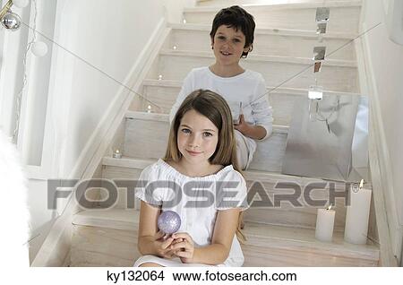 Picture - Little girl sitting indoors, holding a Christmas ball, indoors. Fotosearch