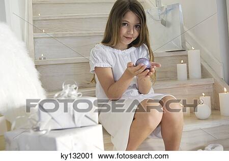 Little girl sitting indoors, holding a Christmas ball, indoors View Large Photo Image Stock Image - Little girl sitting indoors, holding a Christmas ball, indoors. Fotosearch