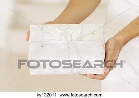 Stock Image - Man hand holding a present, close-up, indoors. Fotosearch