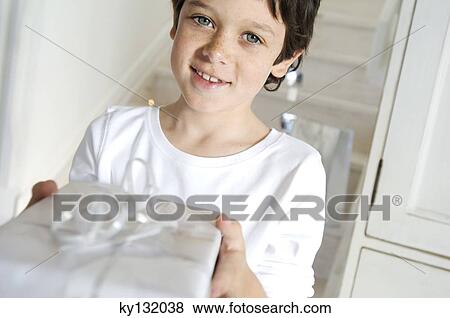 Portrait of a little boy offering a Christmas present, indoors View Large Photo Image Stock Photo - Portrait of a little boy offering a Christmas present, indoors. Fotosearch
