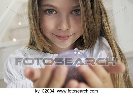 Picture - Portrait of a little girl posing for the camera, holding a Christmas ball, indoors. Fotosearch