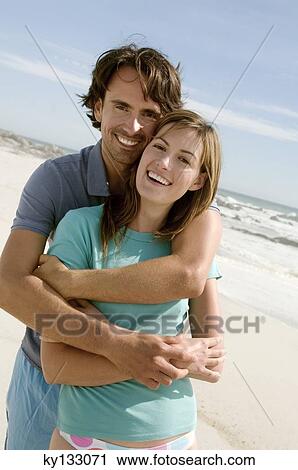 Stock Image - Couple in an embrace, on the beach, posing for the camera, outdoors. Fotosearch