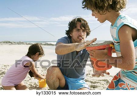 Stock Photography - Father and two children playing on the beach, outdoors. Fotosearch