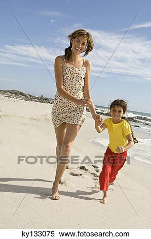 Stock Photography - Mother and daughter walking on the beach, outdoors. Fotosearch