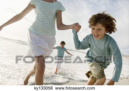 Stock Photo - Mother and two children running on the beach, outdoors. Fotosearch
