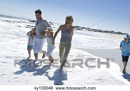 Stock Photograph - Parents and three children walking on the beach, outdoors. Fotosearch