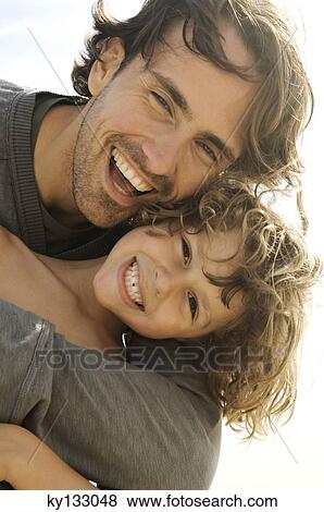 Stock Photo - Portrait of a father and son smiling, looking at the camera, outdoors. Fotosearch