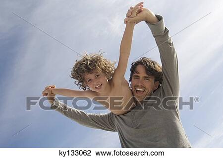 Stock Image - Portrait of a father carrying his son on his back, outdoors. Fotosearch
